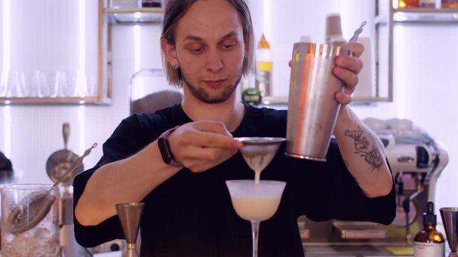 Mixing drink. Barkeeper strain. Man pouring white liquid ingredient from metal shaker to glass. Professional tool for cocktail technique.