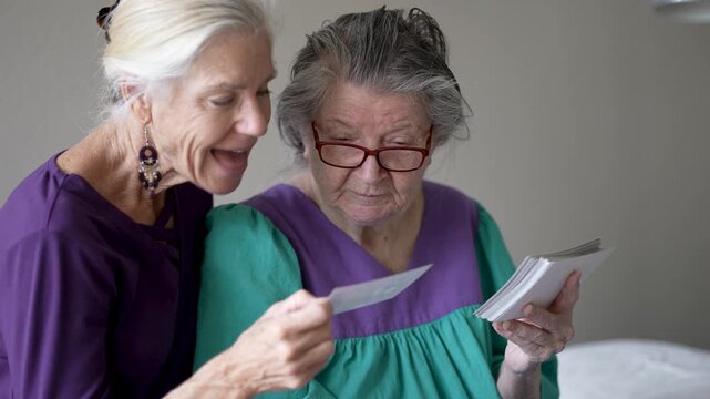Mature daughter spends time with elderly mother in senior care facility looking at photos and sharing stories about their lives