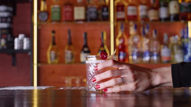 Drink presentation. Cocktail glass. Unrecognizable customer woman hand taking beverage decorating with lemon spiral zest cherry on bar counter.