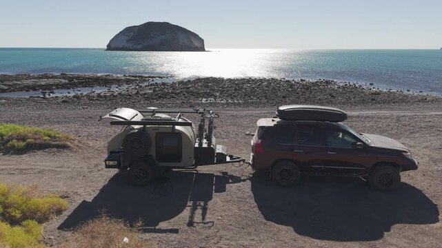 Suv and teardrop camper parked by the beach at sunrise on the Sea of Cortez in Baja California while camping with family.