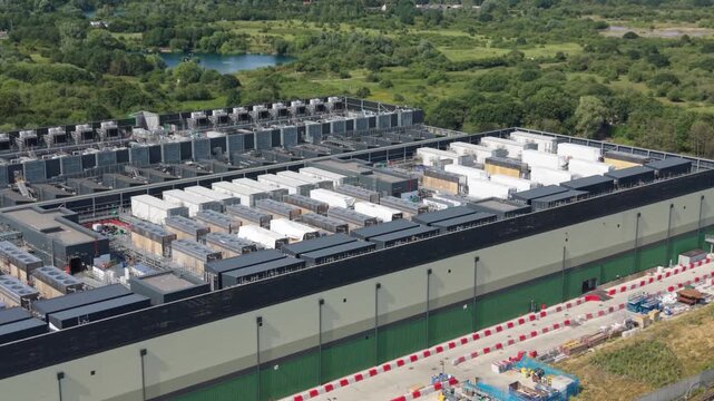 Aerial view of a large data center facility with numerous cooling units on the roof and surrounding green space in London, London, United Kingdom.