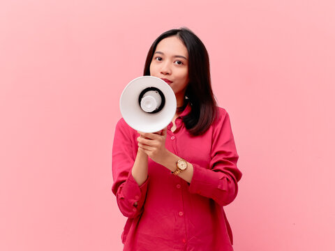 A portrait of a young Asian woman holding a white megaphone to her mouth to make a loud announcement.
