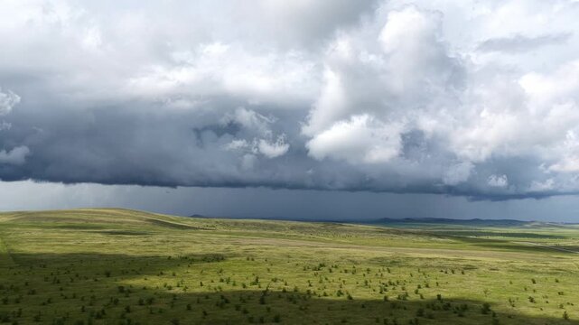 Dramatic storm clouds gathering over vast green hills and wilderness plains before heavy rain, atmospheric panoramic landscape of approaching bad weather in the valley.