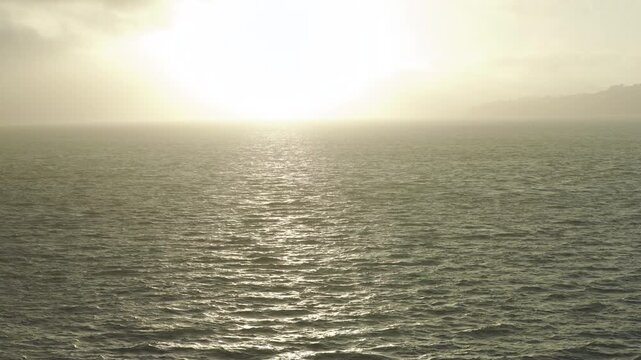 Sun Glare Path Across Choppy Ocean With View Of Coastal Hills And Haze