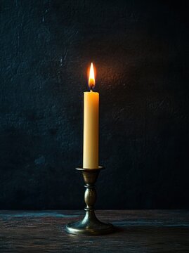 single lit taper candle in brass candlestick on wooden table against dark textured wall, warm glow evoking solitude and calm