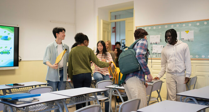 Group of diverse gen z students gathering in classroom, preparing for school lesson