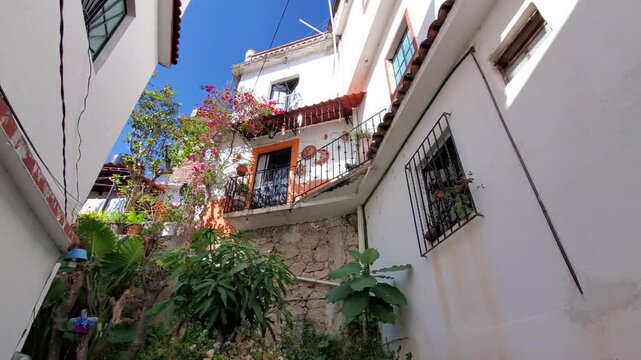 View of a narrow alleyway in Taxco featuring white colonial buildings, vibrant bougainvillea flowers, stone walls, and wrought-iron balconies in Taxco, Guerrero, Mexico.