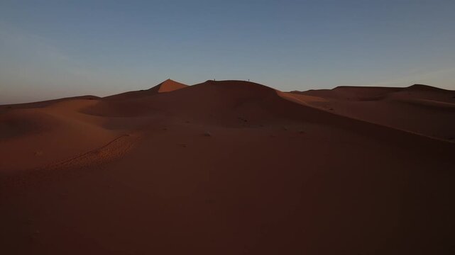 Erg Chebbi dunes stretch across the Sahara near Merzouga, Errachidia, Dr&acirc;a-Tafilalet, Morocco, Africa, glowing beneath warm sunset light, drone forward flyover shot.