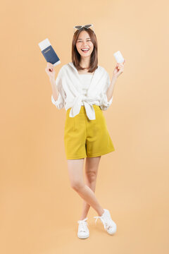 Happy young Asian woman holding smartphone and credit card on orange background, mobile payment and online shopping concept.