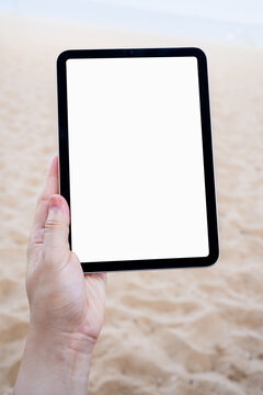 Hand holding tablet with blank screen at the beach for travel, summer vacation and digital technology concept.