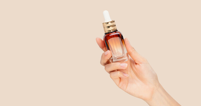 Hands holding glass dropper bottle and using pipette with liquid serum isolated on pastel background for skincare and cosmetic concept.