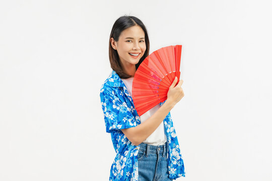Young Asian woman feeling hot and tired while holding a red hand fan and touching her forehead on white background.