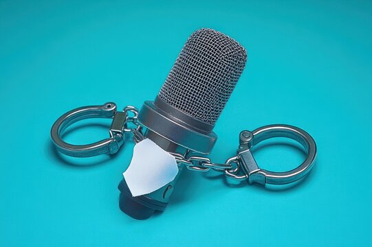 gagged microphone trapped in handcuffs on teal background conveying silenced voice and repression