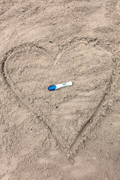 Test de grossesse positif pos&eacute; dans un coeur sur le sable 