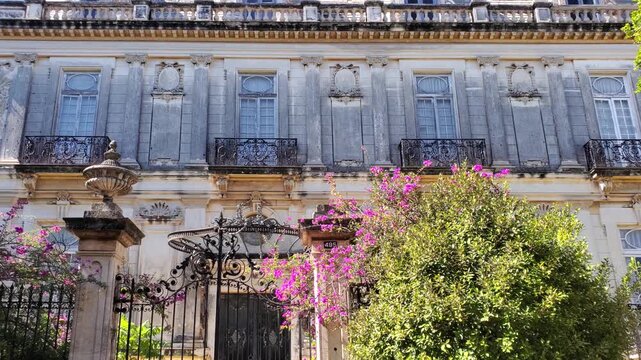 View of the historic mansion on Paseo de Montejo with ornate stone facade, wrought iron balconies, and blooming bougainvillea in Merida, Yucatan, Mexico.
