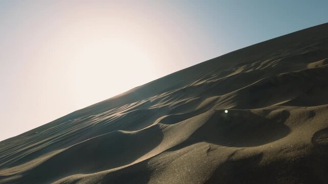 Sunlight illuminating rolling desert sand dunes with natural wind patterns and soft shadows. Minimal arid landscape capturing the beauty, texture, and tranquility of a remote desert environment.