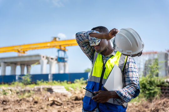 Construction worker man wiping sweat under the hot sun, Exhausted engineer taking a break at construction site in heat, Manual labor in extreme weather, Worker struggling with heat stress