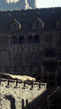 A large stone building stands prominently in a historic setting. Sunlight highlights its aged architecture. The building features multiple windows and intricate designs.