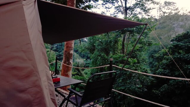 Cozy glamping tent with a shaded outdoor seating area overlooking a lush tropical forest, offering a peaceful nature retreat and scenic camping experience.