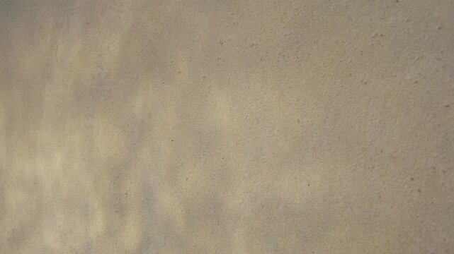 Soft water-like shadows ripple across a textured beige wall, creating a calm abstract background with natural light and gentle flowing patterns.