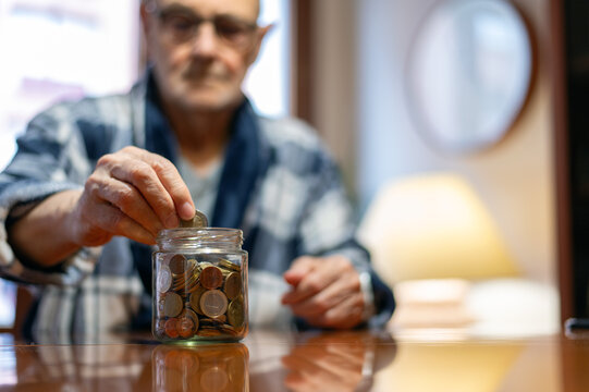 Senior Man Saving Money by Filling a Glass Jar with Coins at Home