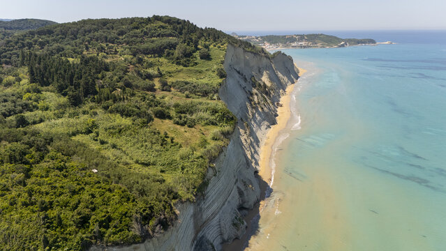 Aerial view of Loggas beach with its dramatic limestone cliffs, lush green vegetation, and turquoise waters along the coastline in Corfu, Greece.