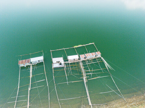 Aerial view of floating fish farms and bamboo structures on the calm green waters of Wadaslintang Reservoir in Wadaslintang, Central Java, Indonesia.
