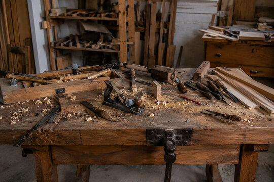 Old carpentry workbench with woodworking tools in workshop background.
