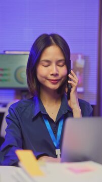 Smiling young Asian businesswoman talking on smartphone in office.