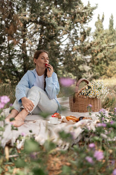 Picnic Flowers Woman: Relaxing woman eats strawberry during daytime picnic with flower basket in forest.