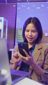 Young Asian woman using smartphone and smiling at mobile screen in home, digital communication and social media concept.