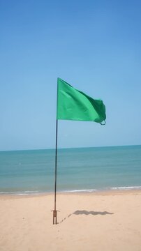 Green safety flag on sandy beach with blue sea and clear sky, safe swimming and coastal tourism.