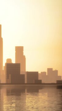 The scene shows a city skyline reflected in water during sunrise. Various buildings are visible, creating a silhouette against the bright sky. The atmosphere suggests early morning time.