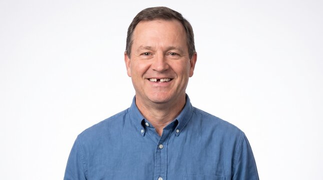 A middle-aged man with a missing front tooth smiles warmly at the camera.