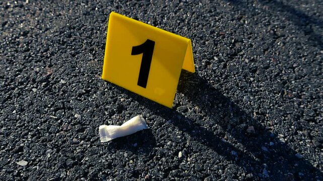 Yellow evidence marker with the number one next to a used white nicotine pouch, representing a clue or proof found on the asphalt road during a police forensic investigation or examination