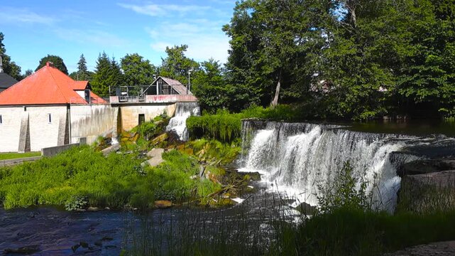 The beautiful Keila Joa waterfall and hydroelectric plant flowing on the Keila river during a sunny summer day in Estonia, a popular european tourist destination with lush green vegetation