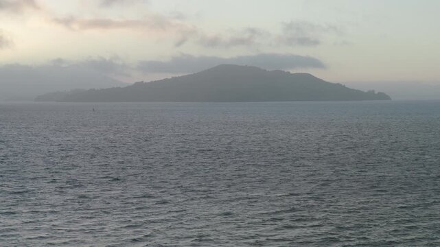 Rising drone shot over choppy San Francisco bay and silhouetted hill in distance at dusk