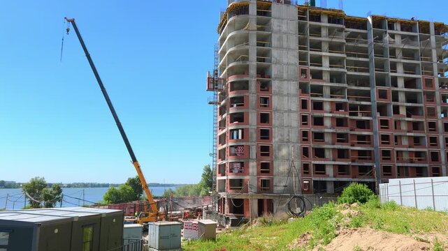 Lifting construction hoist elevator attached to a high-rise residential building under construction near a river on a sunny day