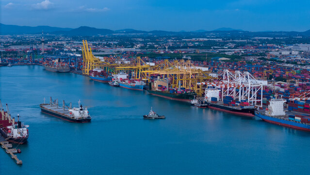 cargo ship guided by tugboats arrives at a massive commercial port terminal featuring gantry cranes and shipping containers, showcasing global maritime logistics and international trade.