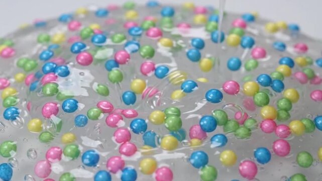 Close up of a finger playing with clear sticky slime filled with colorful pastel foam beads