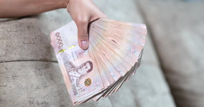 Hand holding Thai baht banknotes, money, cash, representing finance, salary, savings, investment, business, cash flow, and everyday economy concepts