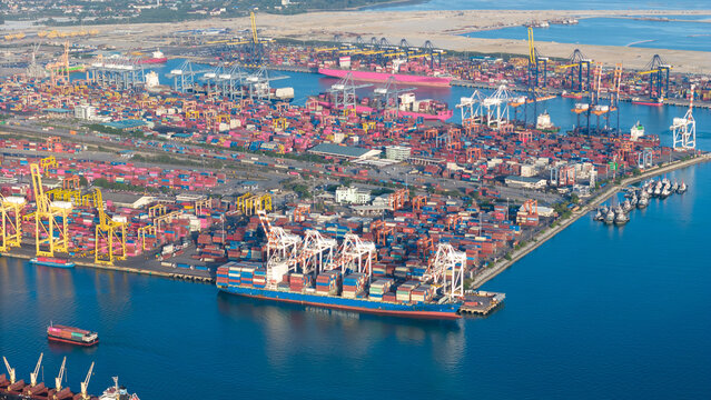 commercial port terminal with cargo ships, container stacks, gantry cranes, storage warehouses, and large car parking lots facilitating global maritime trade and logistics supply chain.