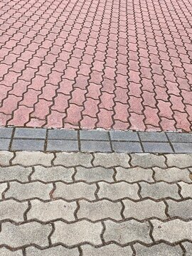 red brick walkway. Interlocking concrete pavement with contrasting red and gray bricks divided by a darker boundary strip for visual separation.