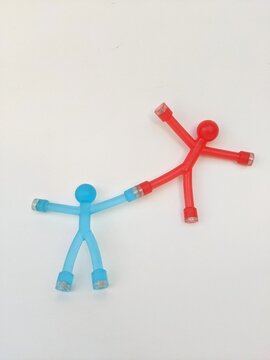 Red and blue suction cup stick figures demonstrate teamwork, support and playful collaboration through connected arms on a light surface. Business metaphor concept