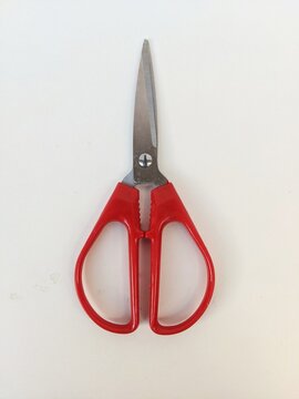 Red-handled scissors with serrated grip and sharp blades, essential household and office cutting tool on white background.