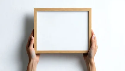 two hands holding a small wooden picture frame with a blank white insert against a white wall, calm minimalist presentation © tech
