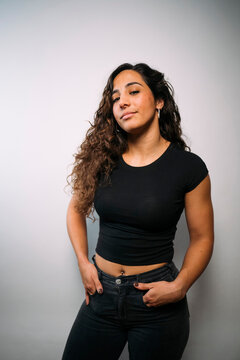 Confident young adult woman posing in studio with hands in pockets