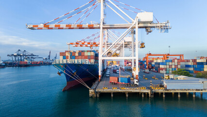 Naklejka premium gantry cranes loading cargo container ship at a busy commercial port terminal, with trailer trucks lined up on the dock to support global maritime logistics and supply chain operations.