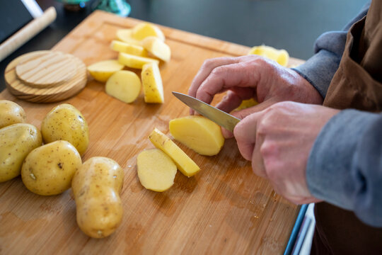 Senior man cutting raw potatoes on cutting board in kitchen