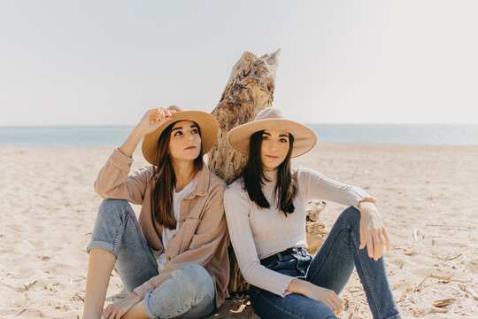 Female twins sitting side by side at beach on sunny day